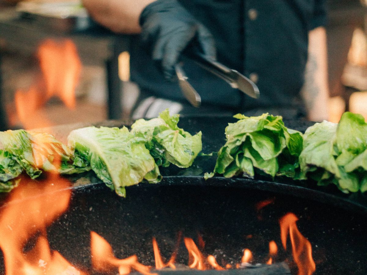 Koch grillt Salatherzen über offenem Feuer auf der Feuerplatte