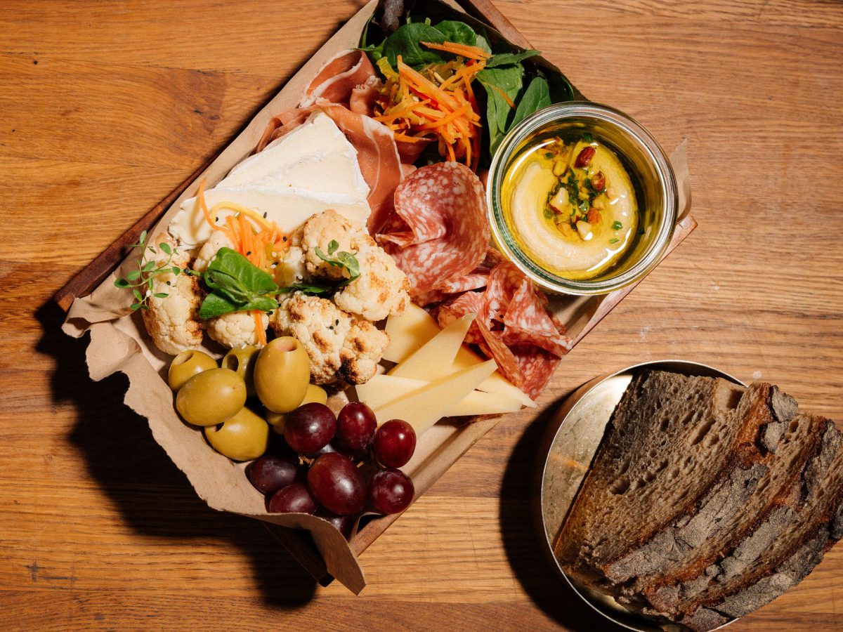 Daily-Who-Box mit Schinken, Käse, Blumenkohl, Oliven und Hummus, daneben Sauerteigbrot