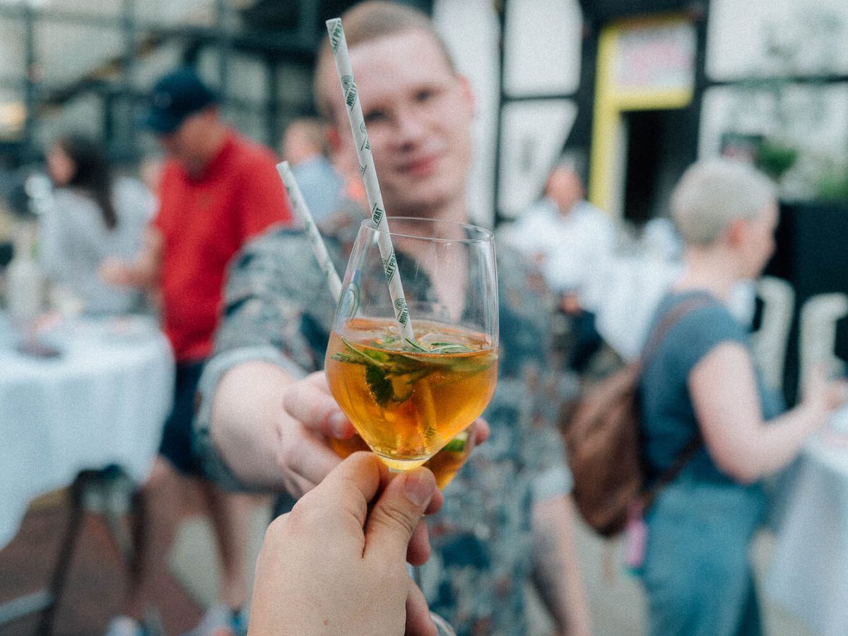 Gast hält ein Glas Spritz beim Empfang in einer Fachwerkhalle