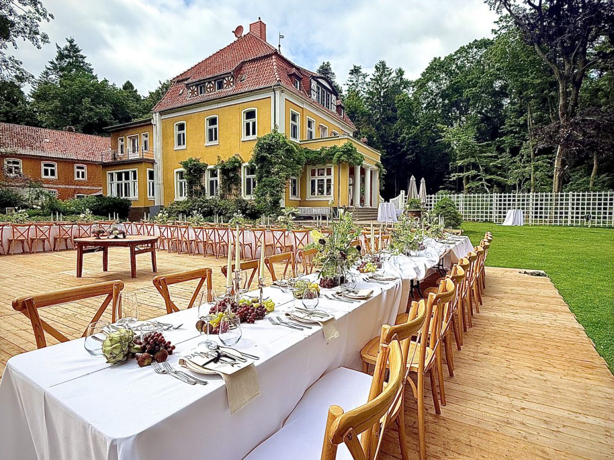 Lange weiße Hochzeitstafel mit Holzstühlen im Garten einer Gutsvilla