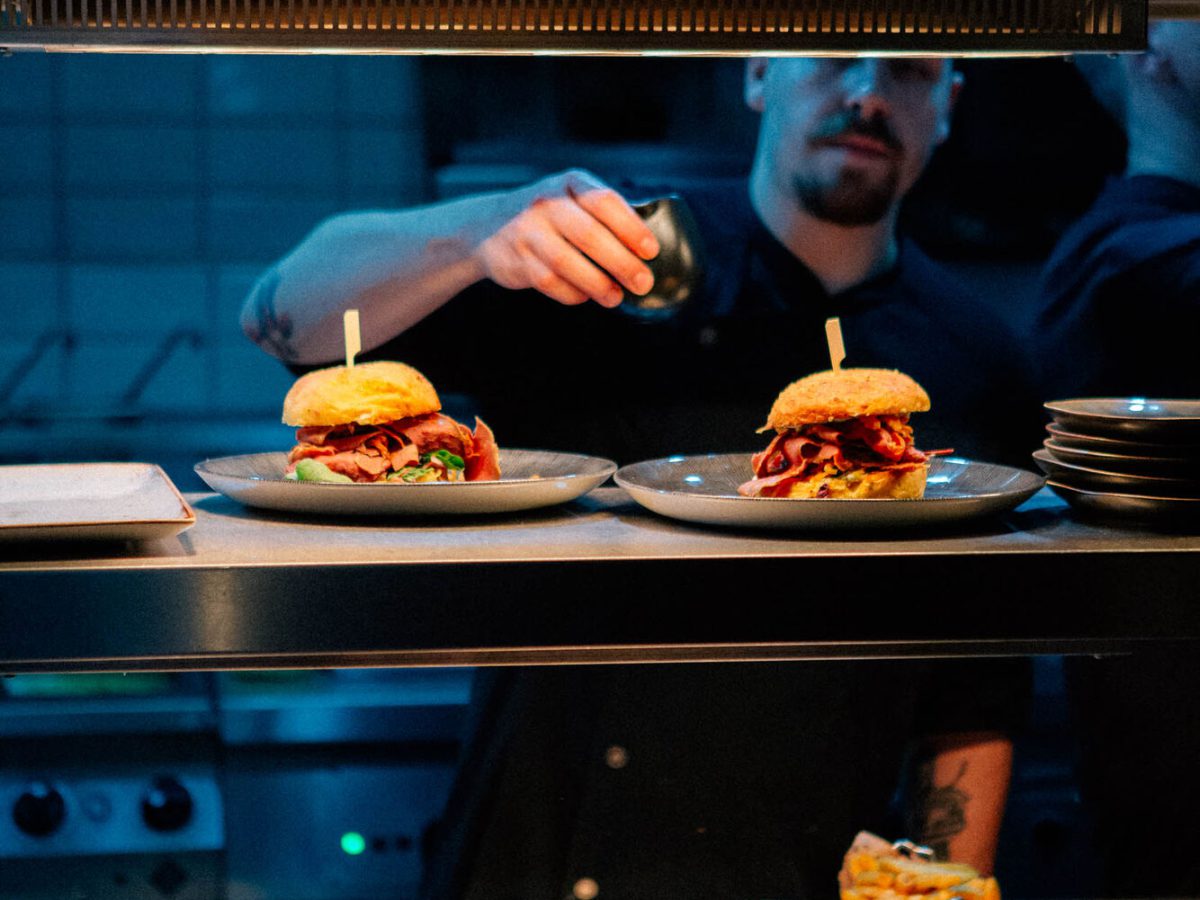 Blick über den Pass in die offene Küche, zwei Burger werden angerichtet