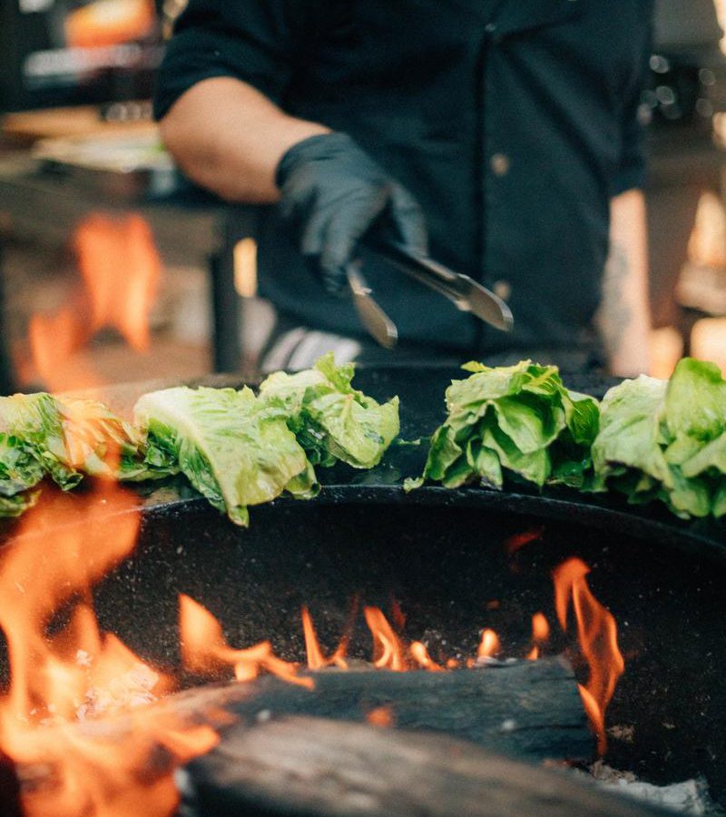 Koch grillt Salatherzen über offenem Feuer bei einem privaten Geburtstagsfest auf dem Landsitz Diek