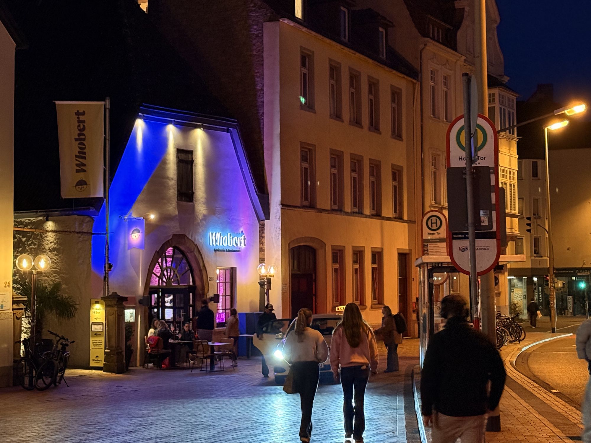 Blau angestrahlte Fassade des Whobert Restaurant am Heger Tor bei Nacht, Passanten auf der Rolandsmauer