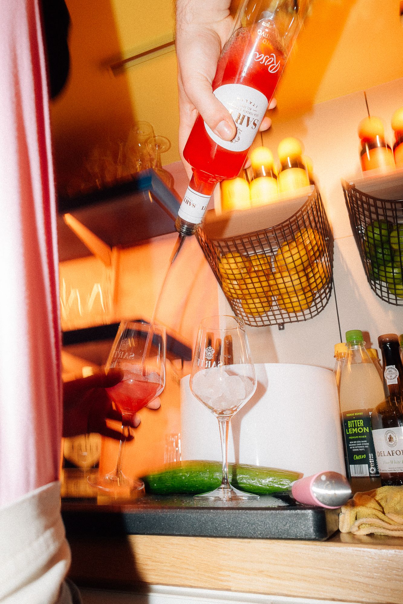 Hinter der Bar wird SARTI Rosa ins Glas gegossen, daneben Zitronen und Limetten