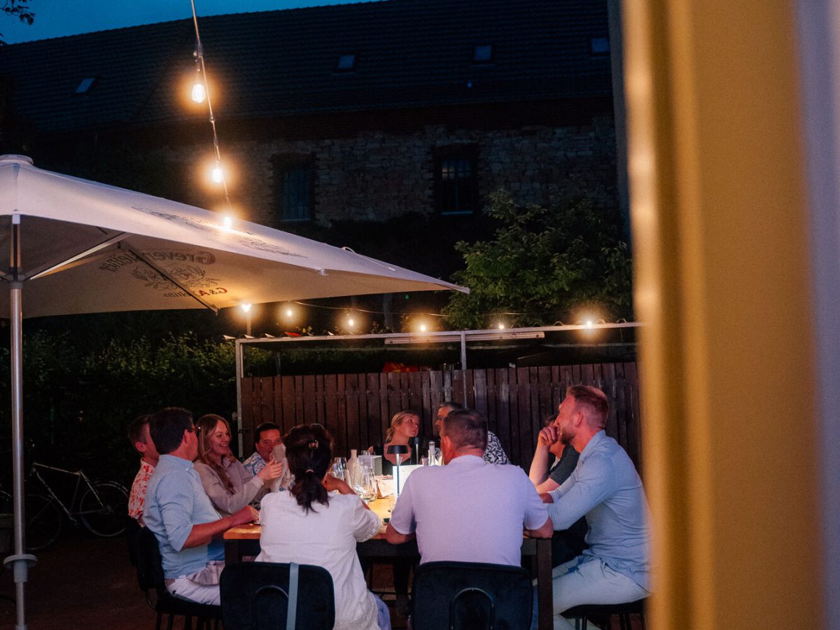 Gäste an einer langen Tafel auf der Terrasse unter Lichterketten