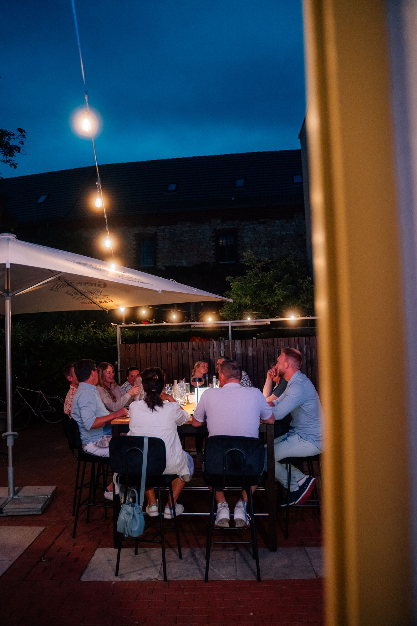 Gäste an einer langen Tafel auf der Terrasse unter Lichterketten