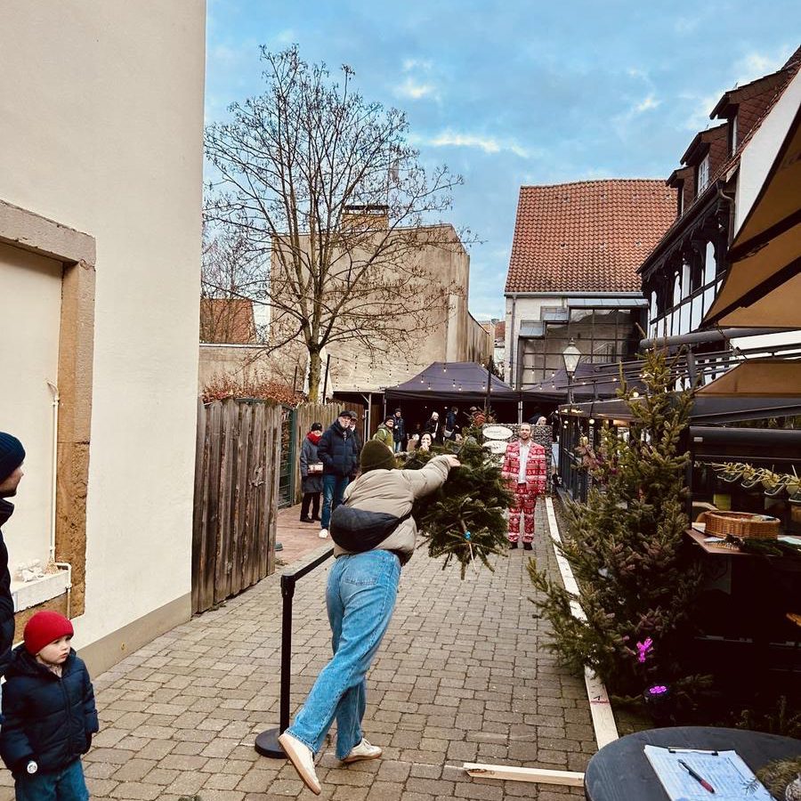 Gast wirft beim Teambuilding-Wettkampf einen Weihnachtsbaum durch die Gasse vor dem Whobert, Zuschauer feuern an